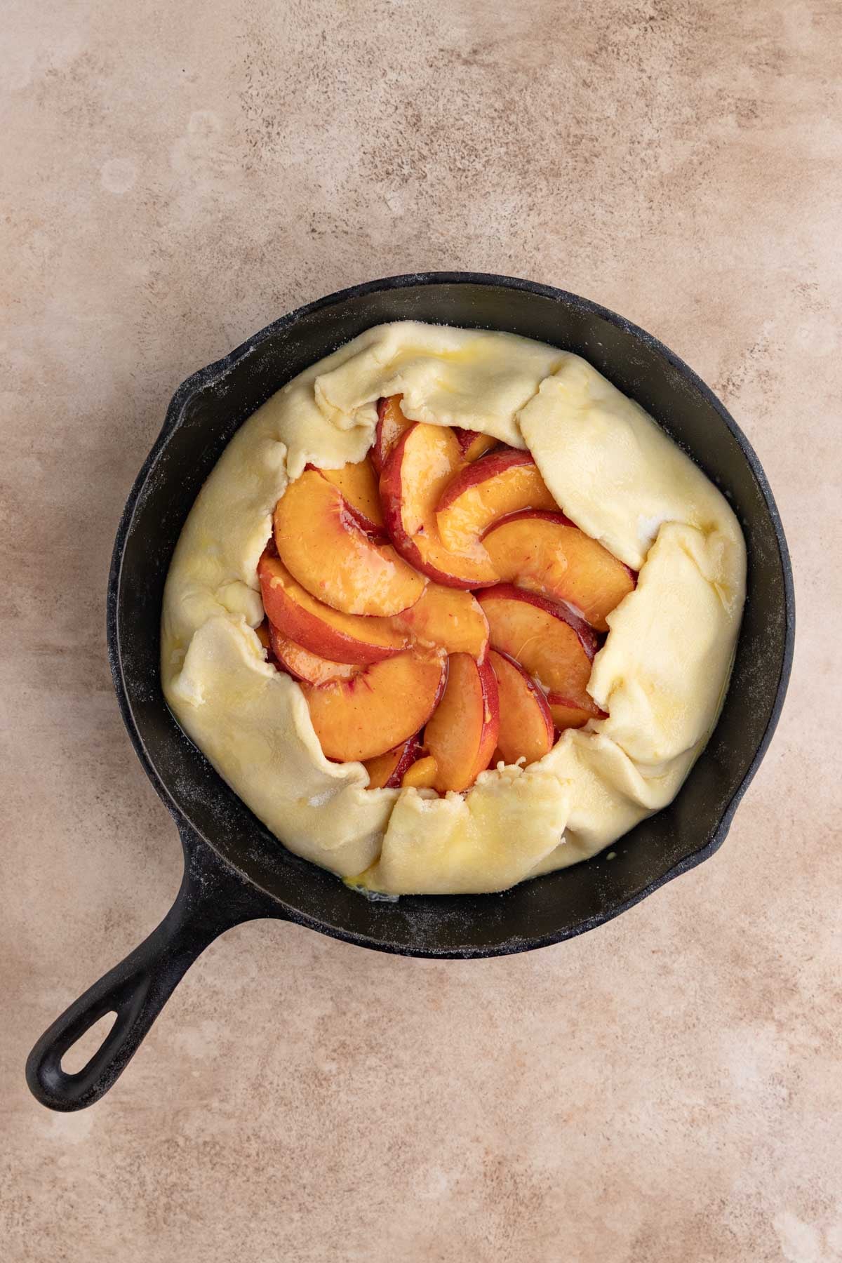 Unbaked peach galette in the cast-iron pan. The edges of the dough are partially pulled over the peaches