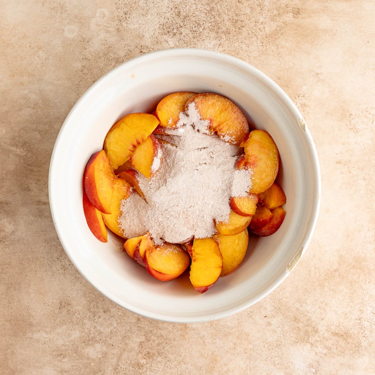 A combination of sugar, tapioca, cinnamon and nutmeg on top of fresh peaches in a ceramic bowl