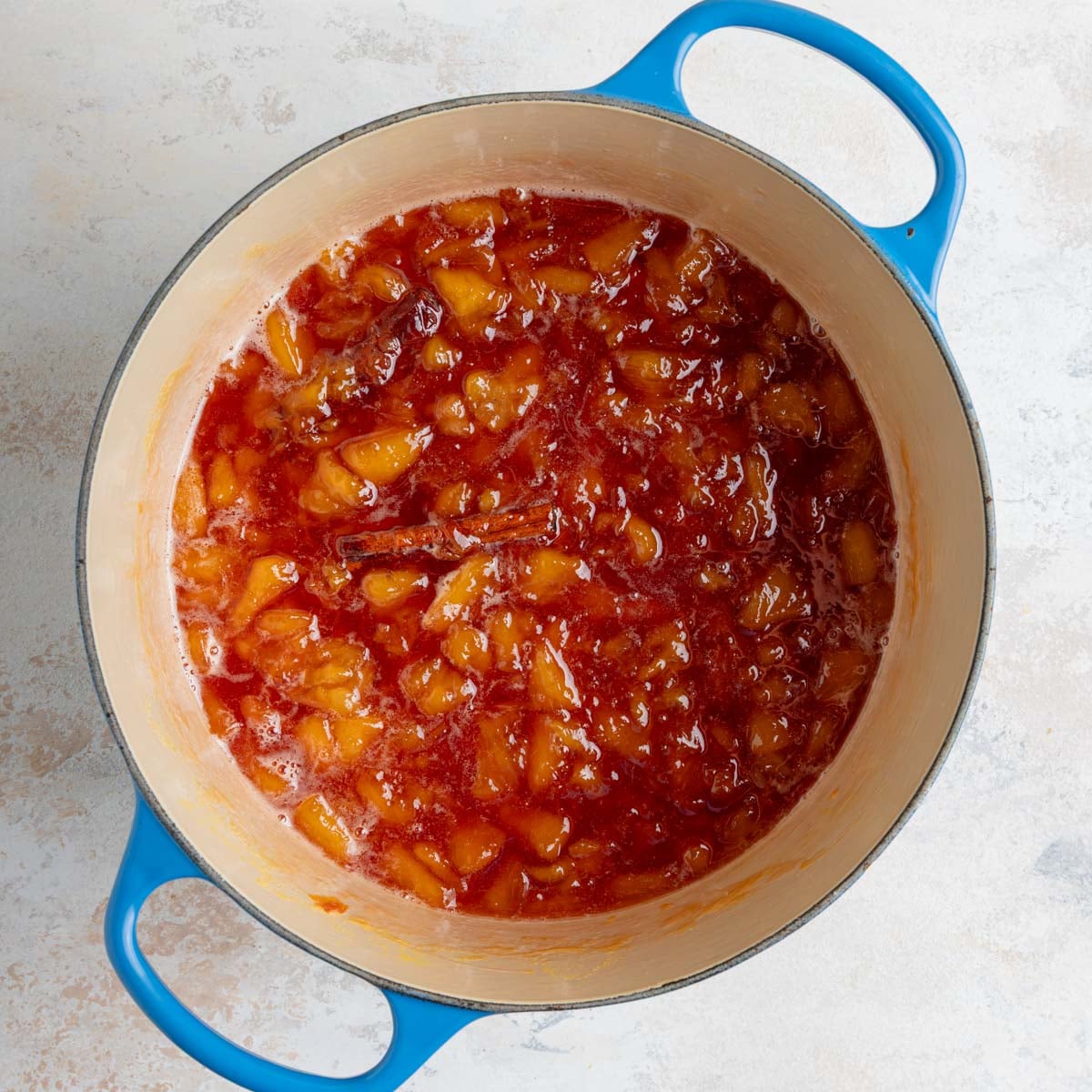 The peach jam in an enameled lined pot. Part of the jam has been smashed and is partly chunky.