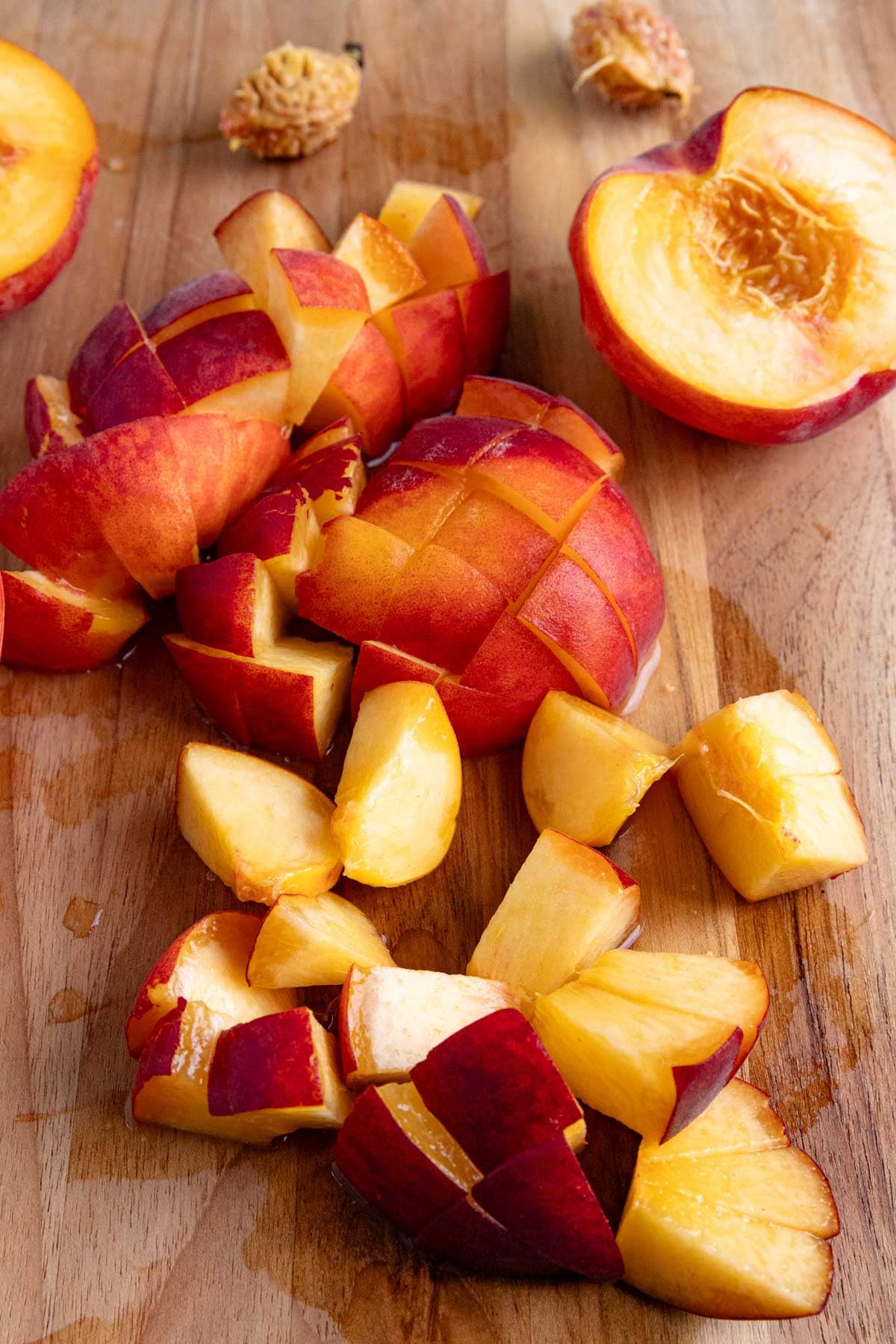Chopped peaches on a wooden board with two half peaches also on the board