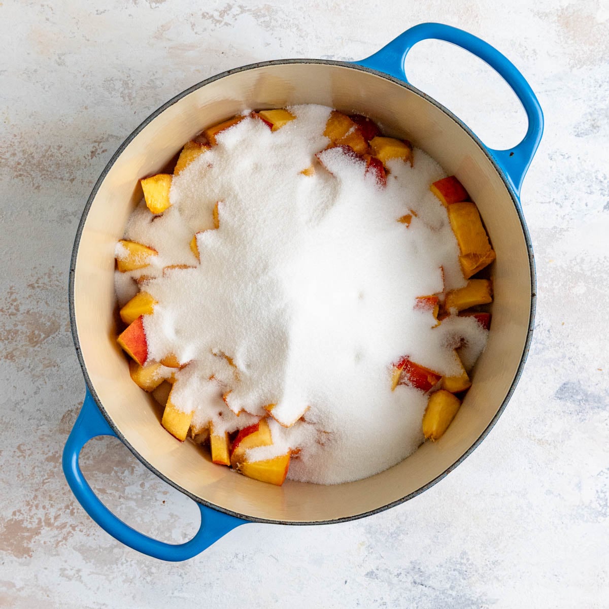 Chopped peaches with granulated sugar in an enameled lined pot