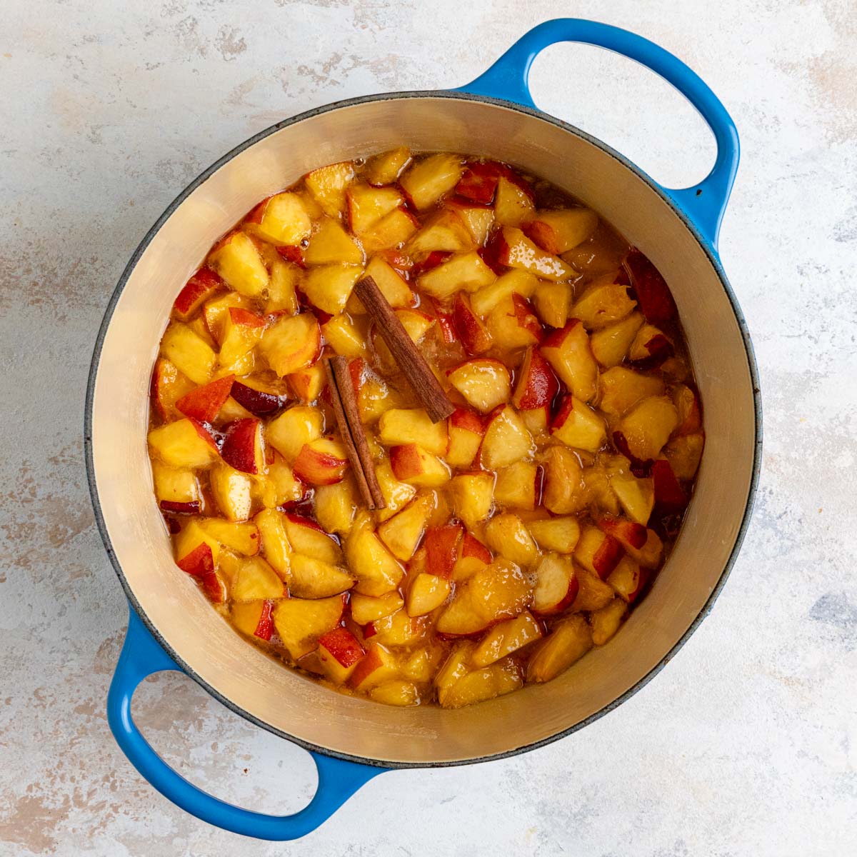 Macerated peaches in an enameled pot with cinnamon sticks