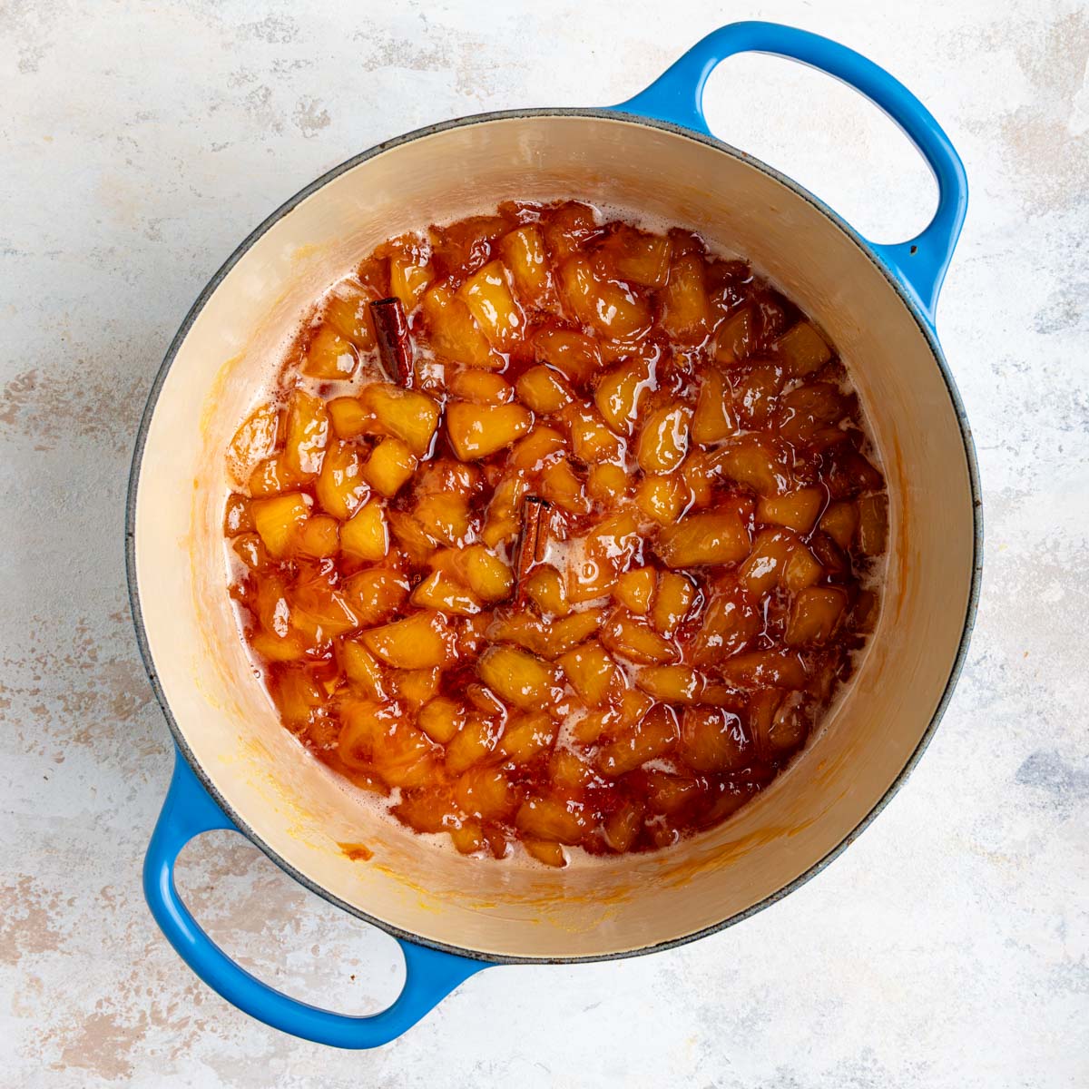 Cooked peach jam in an enameled lined pot. The jam is chunky and has a deep orange color