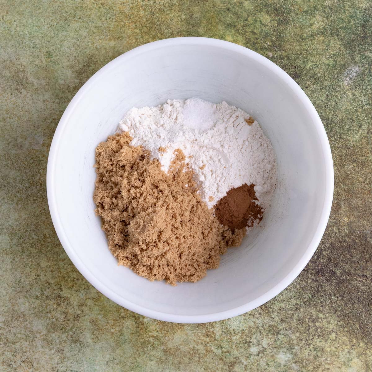 Brown sugar, flour, cinnamon, cardamon, and nutmeg in a ceramic mixing bowl.