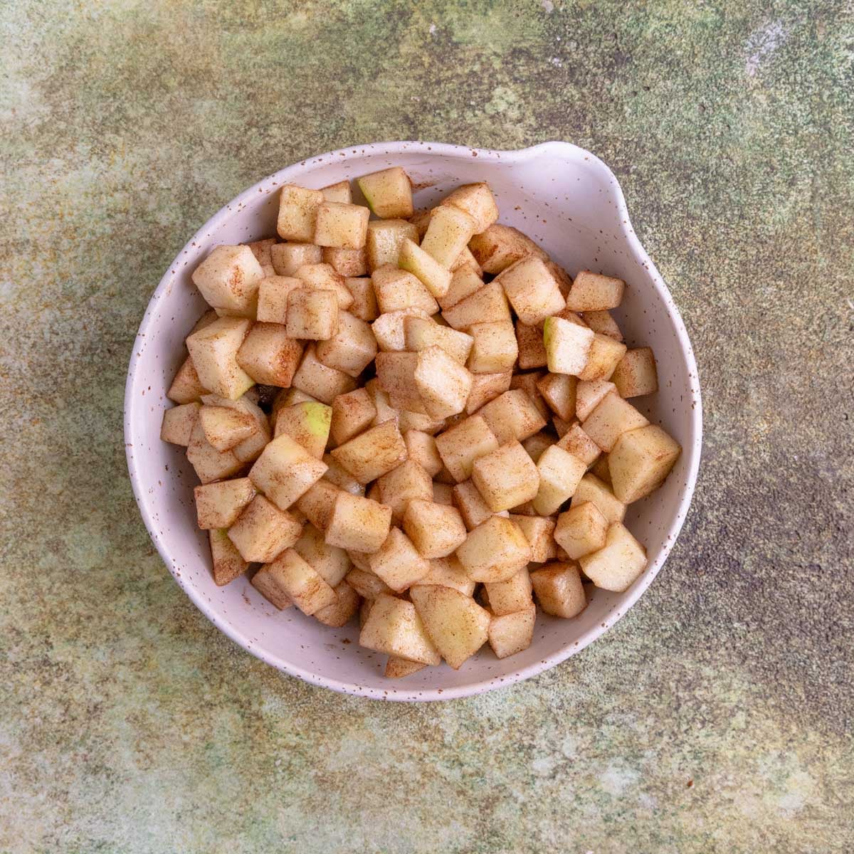 Chopped apples coated with cinnamon and sugar in a small ceramic bowl.