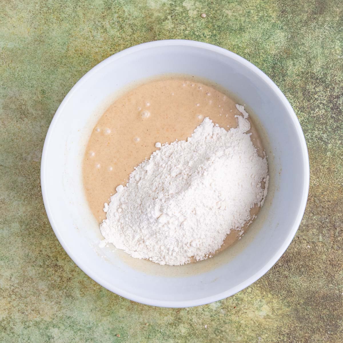 Muffin batter in a ceramic bowl with the flour mixture added