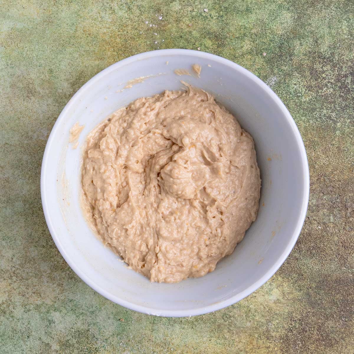 Muffin batter in a ceramic mixing bowl. The batter is light brown and appears thick.