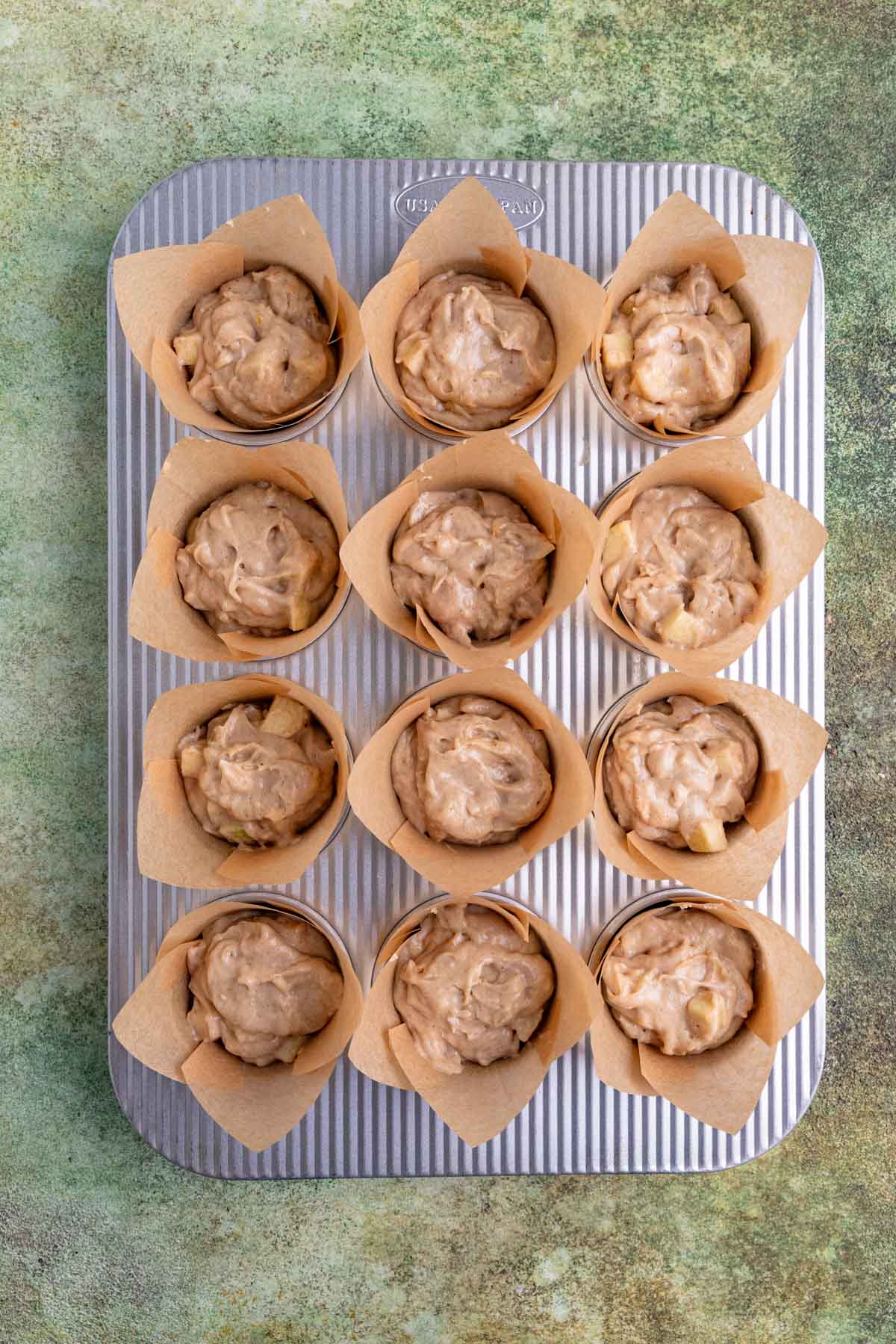 Muffin batter divided between 12 tulip cupcake liners in an aluminum muffin pan