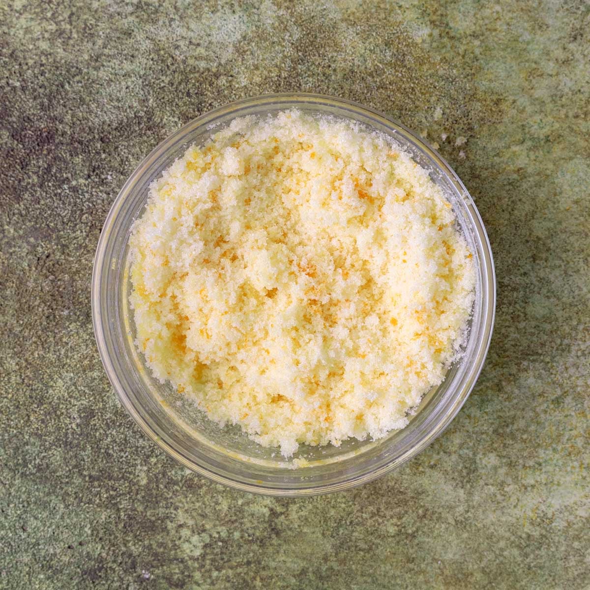 Orange zest mixed into sugar in a small glass bowl. The mixture is light orange in color