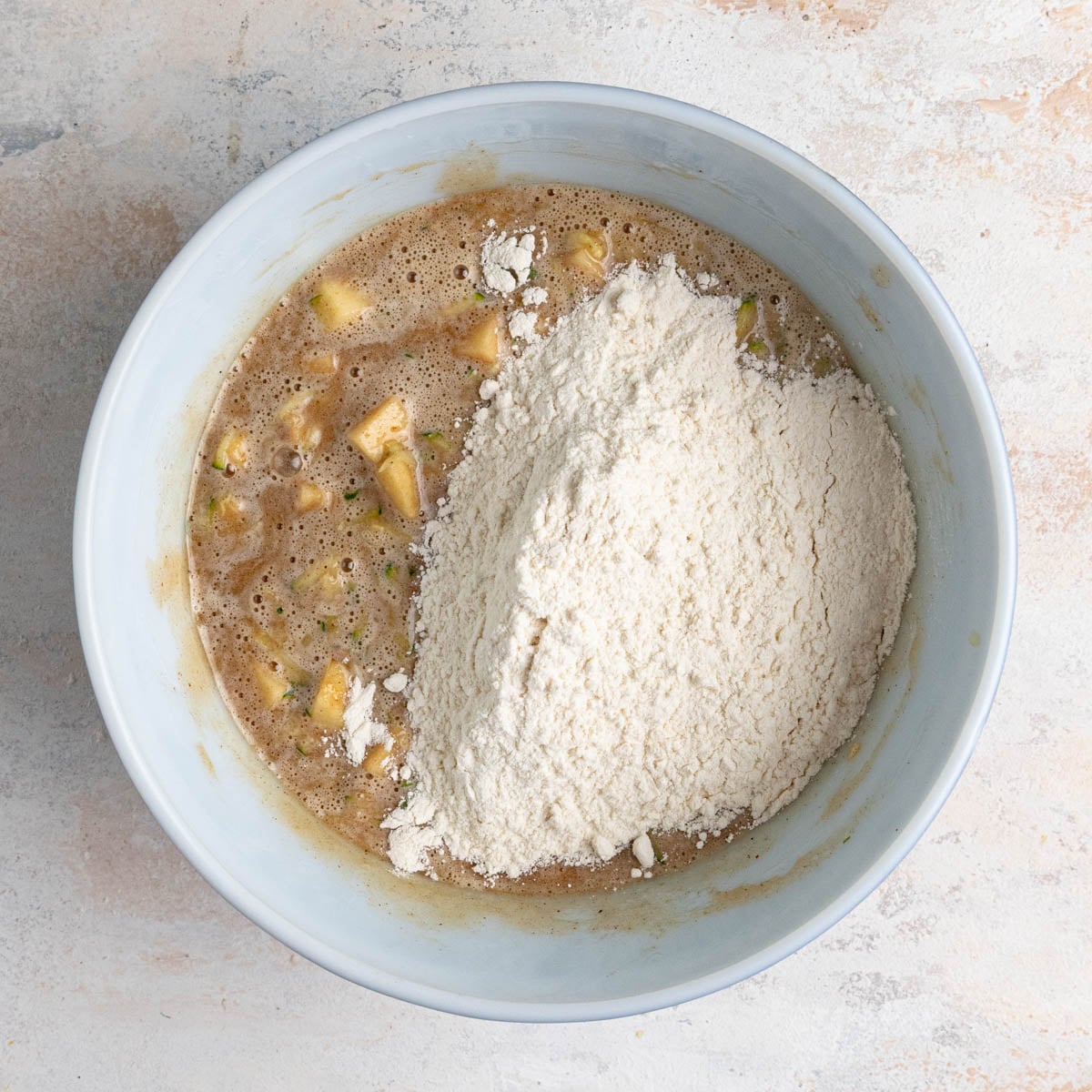 The zucchini bread batter in a white ceramic bowl with the flour flour mixture added and sitting on top