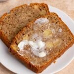 A slice of apple zucchini bread with butter spread on top sits on a white plate. A bowl of butter are visible in the background.