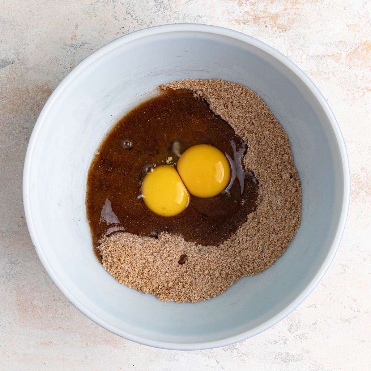 A white ceramic mixing bowl filled with a sugar spice mixture with two large eggs on top of the mixture