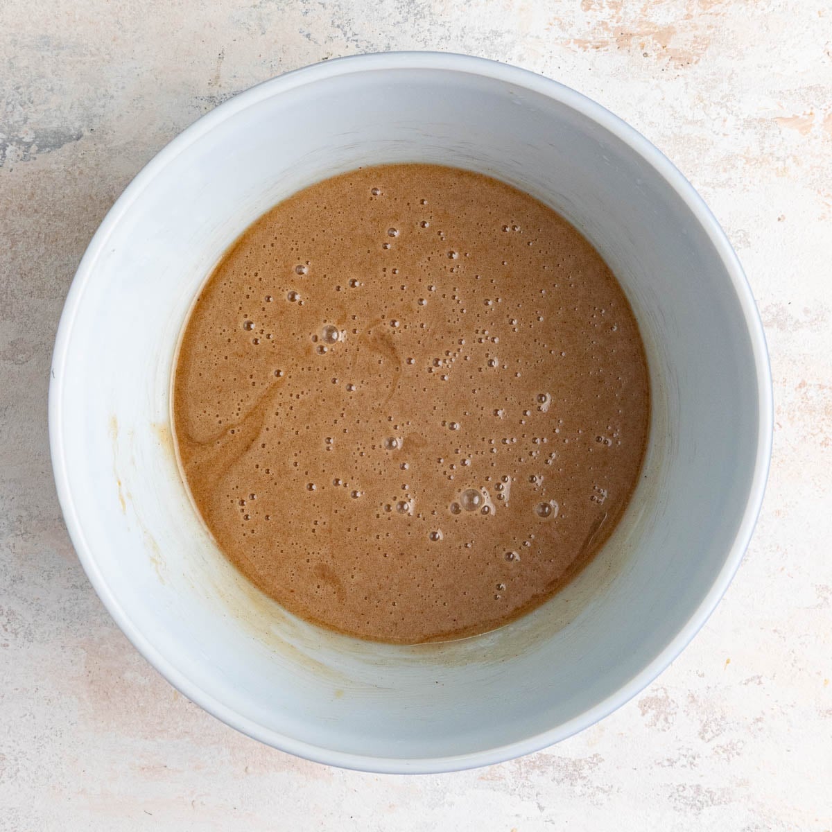 The zucchini batter consisting of the sugar, spices, and two eggs in a white ceramic.