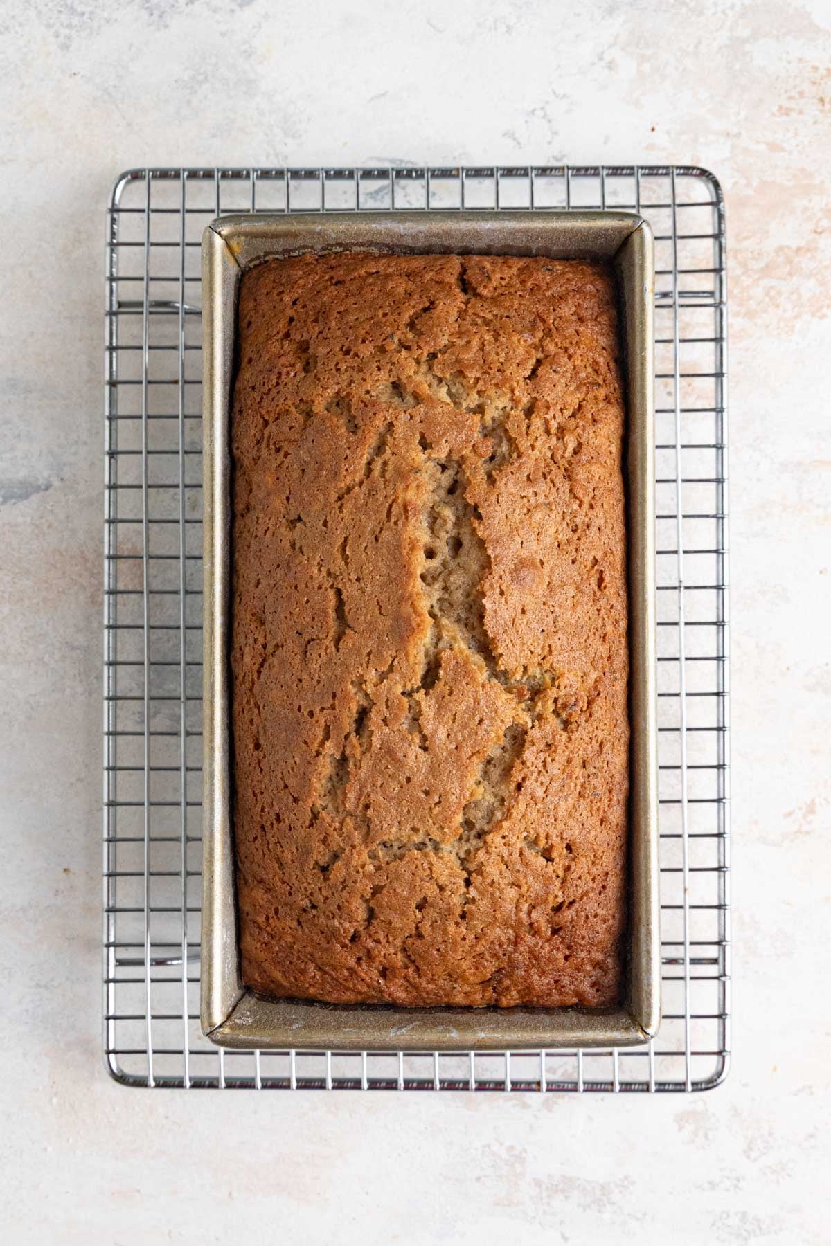 A loaf of zucchini bread sits in a rectangular metal loaf pan on a wire cooling rack.