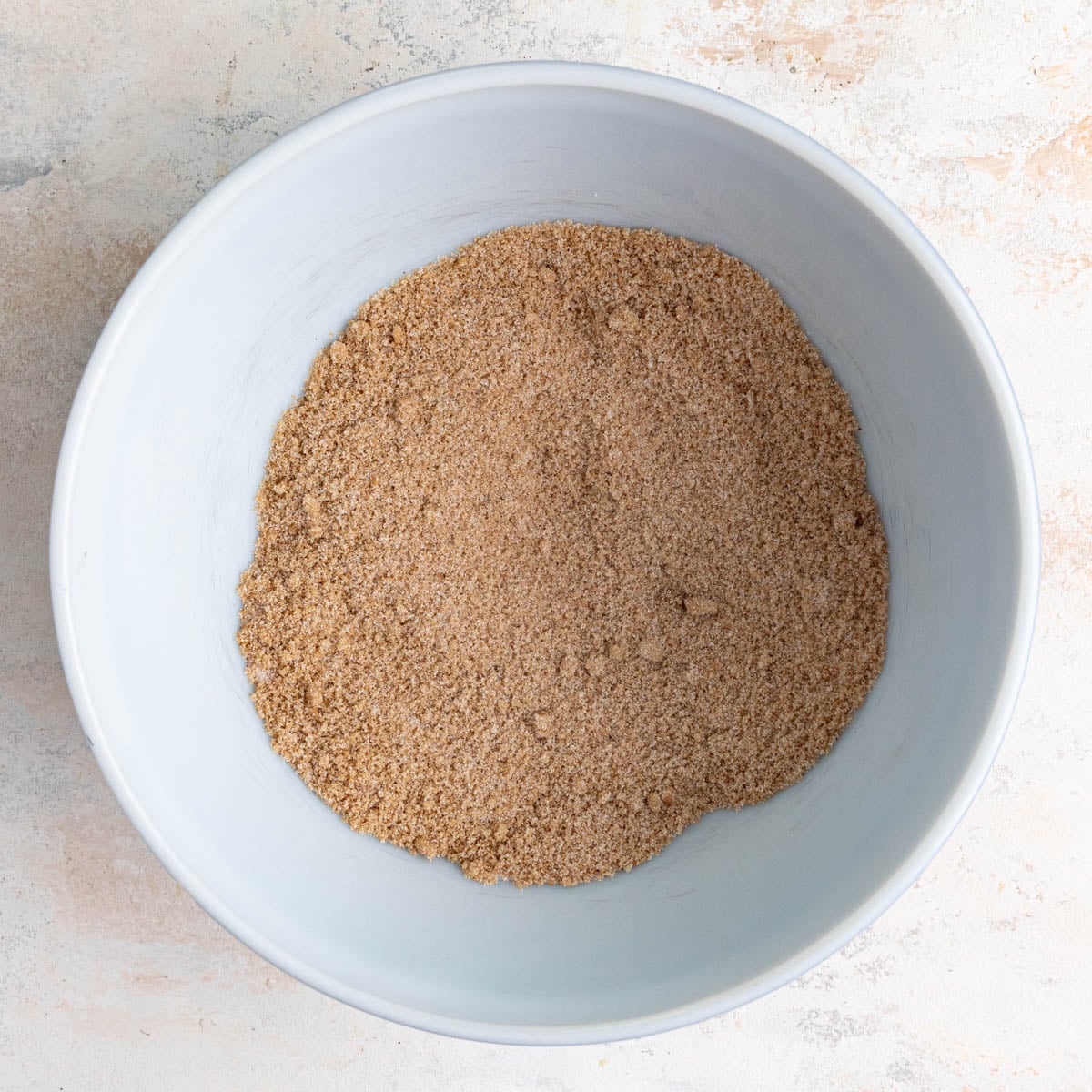 A white ceramic bowl filled with a mixture of brown sugar, granulated sugar, ground cinnamon, ground nutmeg, and ground cloves