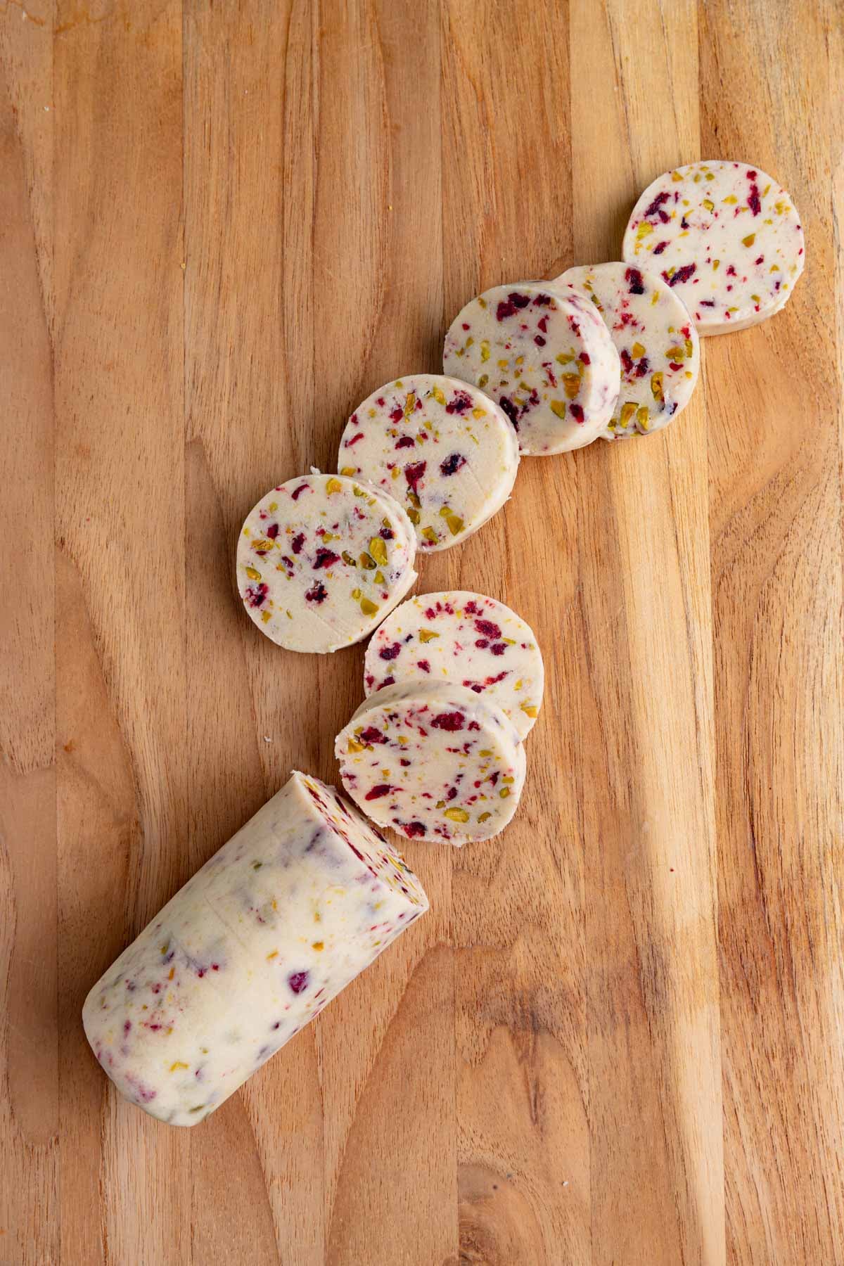 A cranberry pistachio cookie dough log with seven 1/2-inch thick cut pieces. Each sliced is speckled with chopped pistachios and dried cranberries.