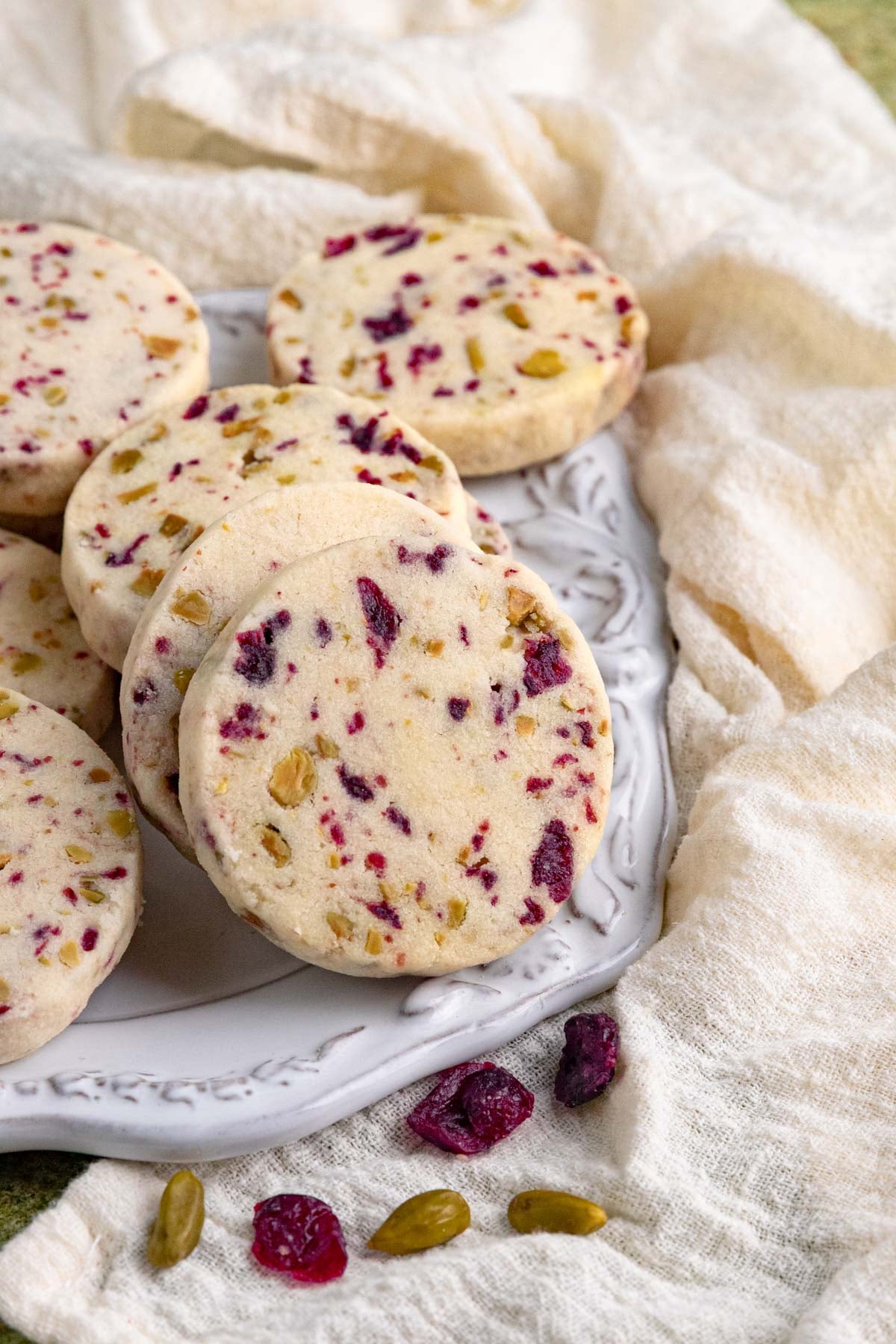 Round shortbread cookies studded with pistachios and dried cranberries on a decorative white plate.