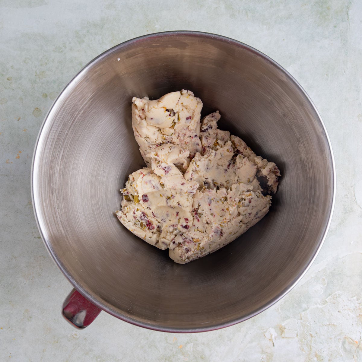 Cranberry pistachio shortbread cookie dough in the bowl of a stand mixer. The dough has flecks of red and green from the pistachios and dried cranberries.