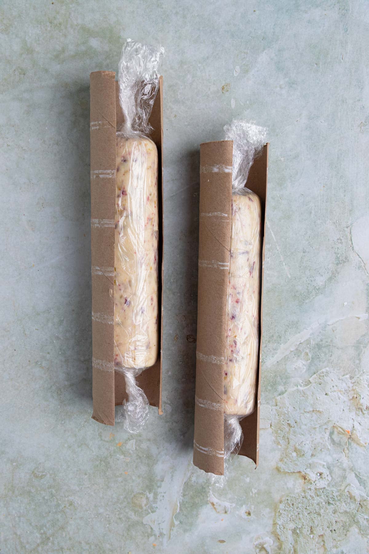 Two dough logs, each wrapped in plastic. Each log is placed inside a paper towel role cut in half length wise.
