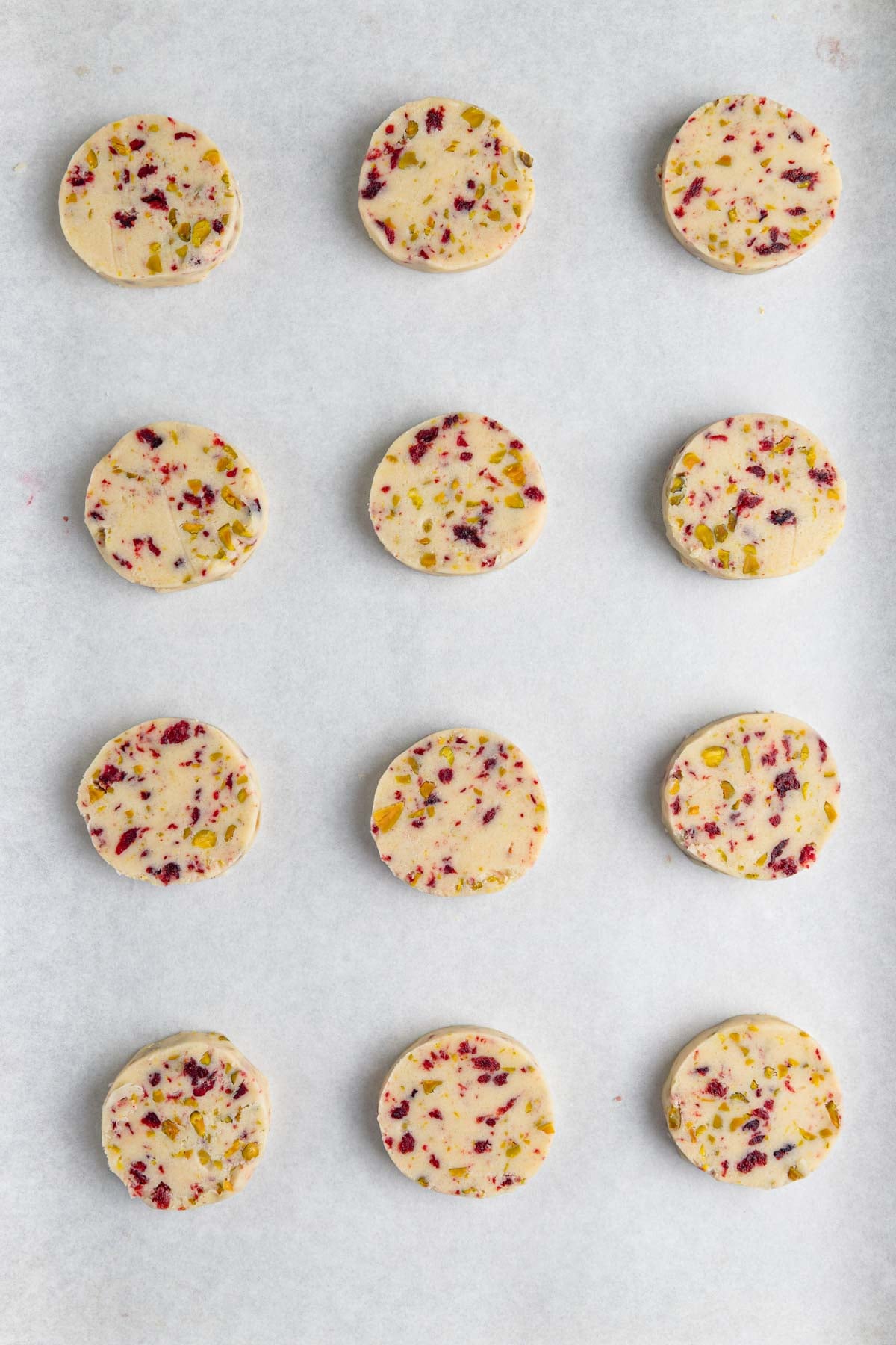 12 unbaked cranberry pistachio shortbread cookies on a parchment lined baking sheet