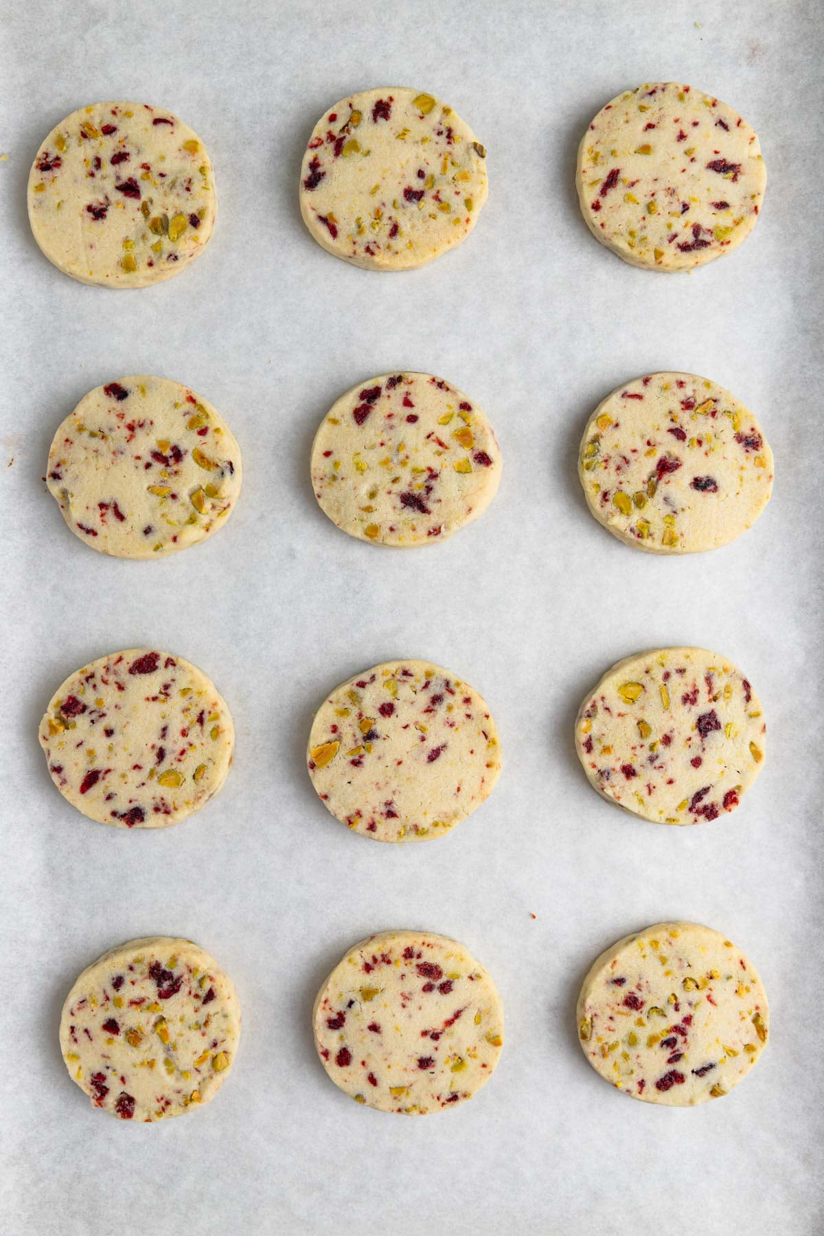 12 baked cranberry pistachio shortbread cookies on a parchment lined baking sheet